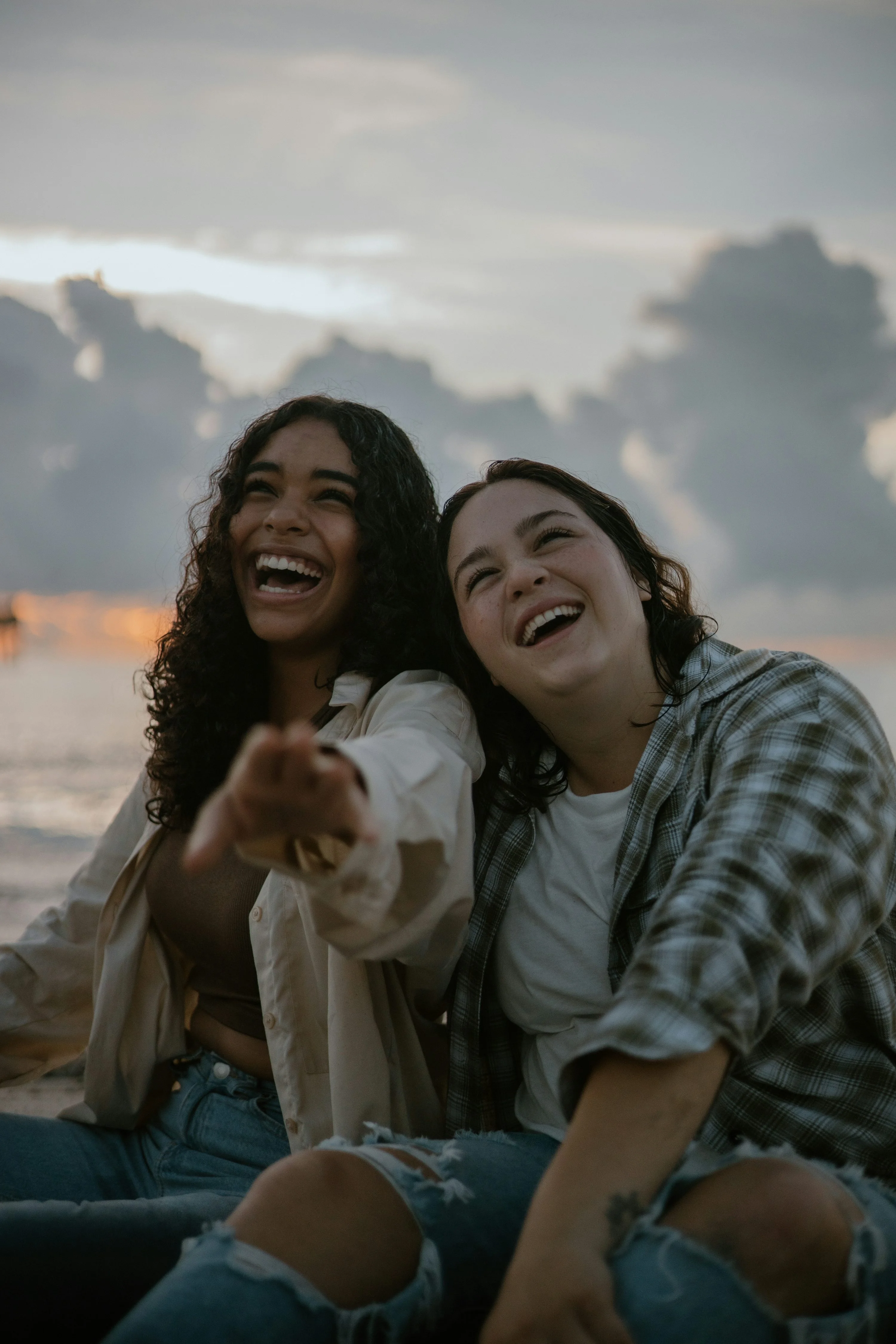Two friends laughing together on a beach at sunset